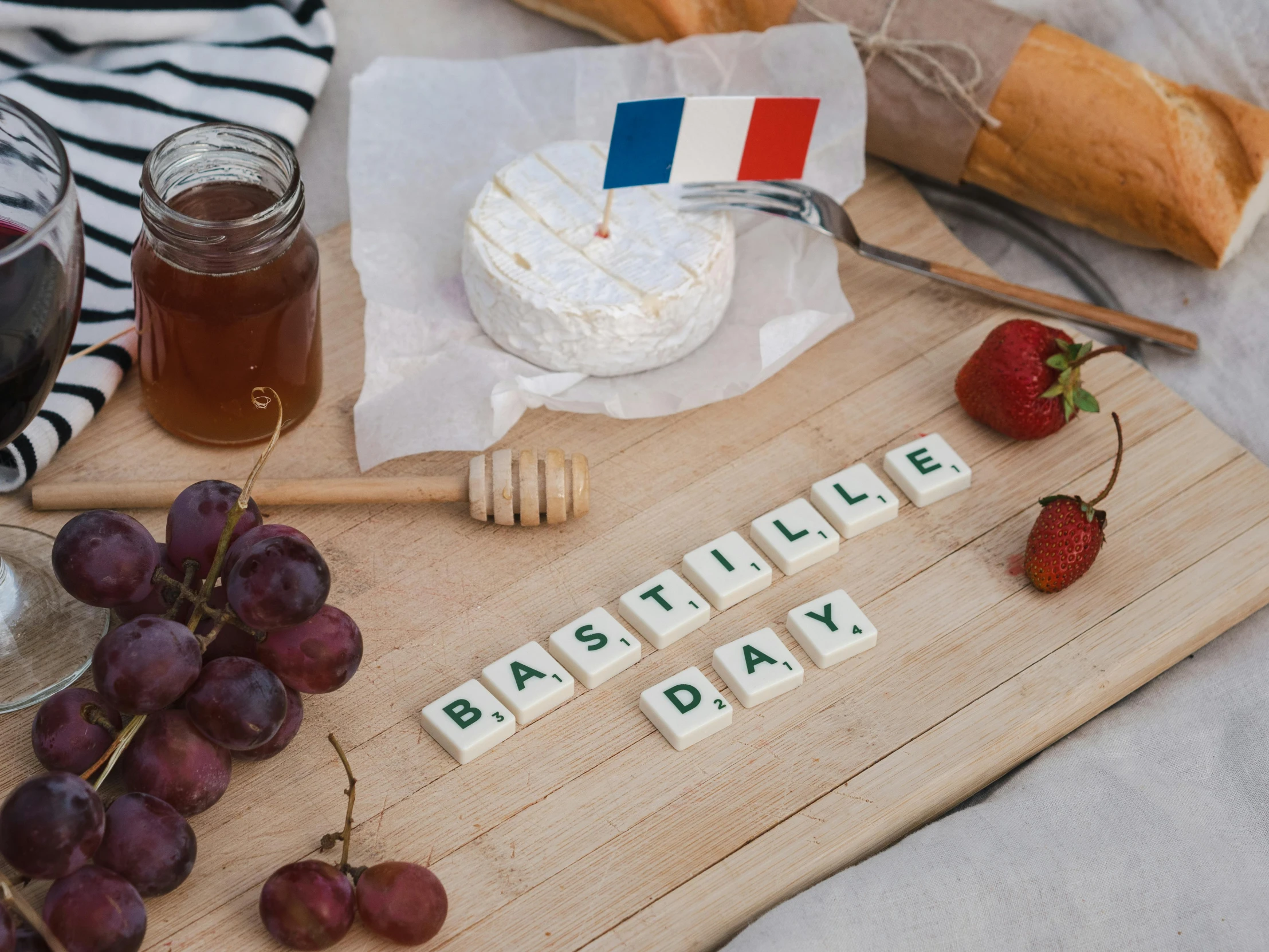 a wooden cutting board topped with fruit next to a glass of wine, inspired by Édouard Detaille, unsplash, letterism, french flag, cheeses, day time, various posed