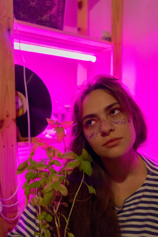 a woman in a striped shirt holding a plant, an album cover, trending on pexels, bright pink purple lights, profile picture, rosalia, low quality photo