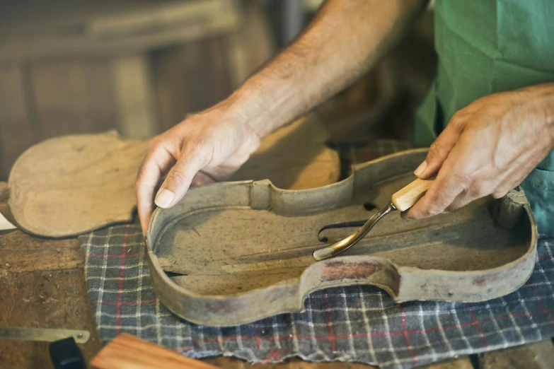 a close up of a person working on a violin, by Jan Kupecký, trending on pexels, arts and crafts movement, working in the forge, on a wooden tray, dressed in a worn, thumbnail