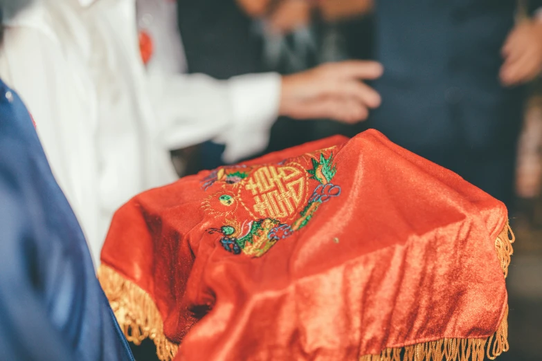 a close up of a person holding a red hat, trending on unsplash, cloisonnism, on the altar, embroidered robes, celebrating an illegal marriage, red tie