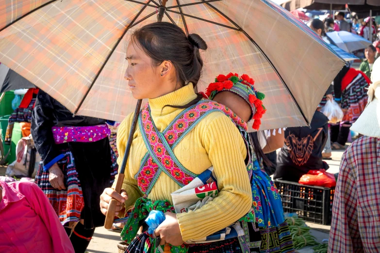 a woman carrying a baby under an umbrella, by Sam Dillemans, pexels contest winner, cloisonnism, wearing authentic attire, square, dao trong le, thumbnail