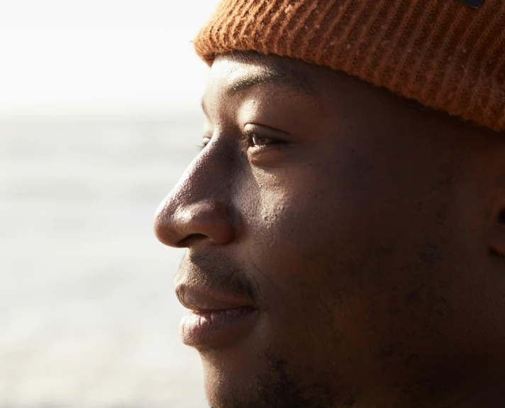 a close up of a person wearing a hat, trending on pexels, looking to his side, with brown skin, gazing off into the horizon, wearing beanie