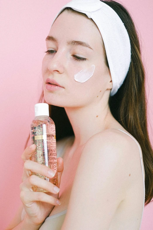 a woman holding a bottle of lotion in front of her face, by Julia Pishtar, trending on pexels, renaissance, glitter accents on figure, taejune kim, pink skin, looking from shoulder