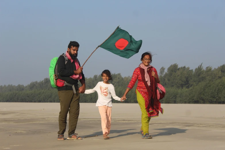 a group of people standing on top of a sandy beach, hurufiyya, indian flag, husband wife and son, walking towards the camera, green flag