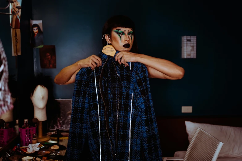 a man that is standing in front of a mirror, an album cover, by Julia Pishtar, trending on pexels, tartan garment, huge earrings and queer make up, costume with blue accents, performance art