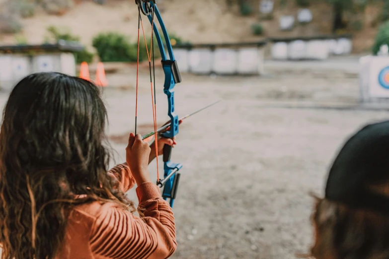 a woman holding a bow and aiming at a target, pexels contest winner, adventure playground, school class, 🦩🪐🐞👩🏻🦳, panoramic view of girl