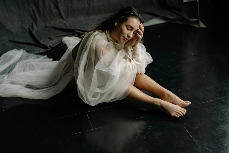 a woman in a white dress sitting on the floor, an album cover, by Emma Andijewska, pexels contest winner, renaissance, solemn gesture, flowing cape, epk, soft skin