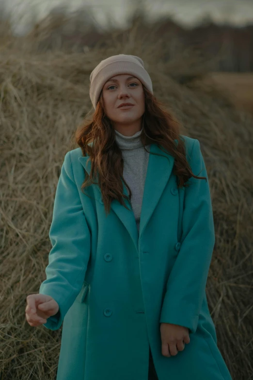 a woman in a blue coat standing in a field, trending on pexels, ( redhead, low quality footage, seafoam green, casual clothing