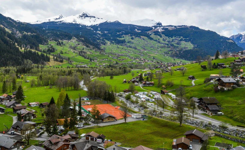 an aerial view of a village in the mountains, pexels contest winner, grass field surrounding the city, swiss modernizm, slide show, snow capped mountains