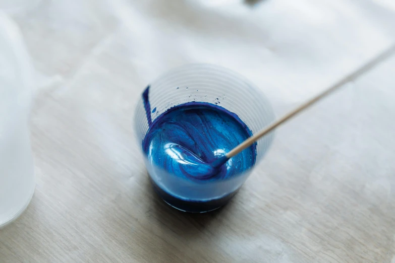 a cup of blue liquid with a toothpick sticking out of it, inspired by Yves Klein, unsplash, process art, metallic paint, swirling fabric, modelling clay, blueberry and orange and teal