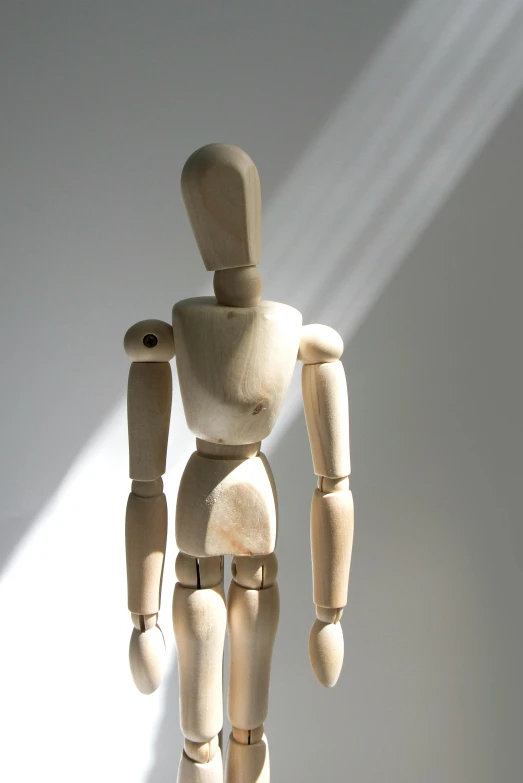 a wooden mannequin standing in front of a white wall, articulated joints, sunlight beaming down, looking confused, dimly lit