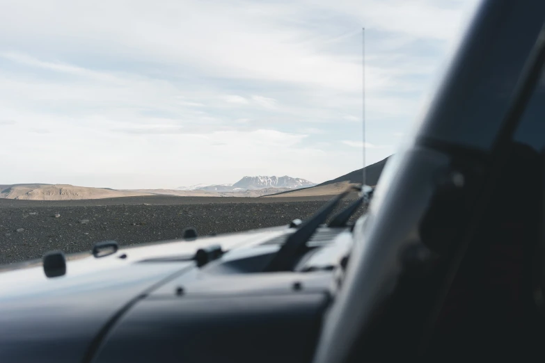 a close up of a car window with mountains in the background, by Jeffrey Smith, unsplash, hurufiyya, black volcano afar, soft top, off - road, sparse mountains on the horizon