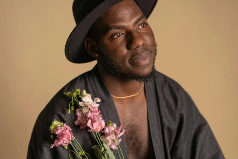 a man with a hat holding a bouquet of flowers, inspired by Theo Constanté, pexels contest winner, black arts movement, non binary model, wearing brown robes, loveable guy, black skin