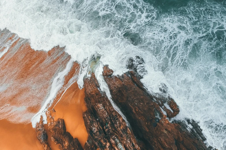 a person riding a surfboard on top of a sandy beach, pexels contest winner, erosion algorithm landscape, helicopter view, orange rocks, south african coast