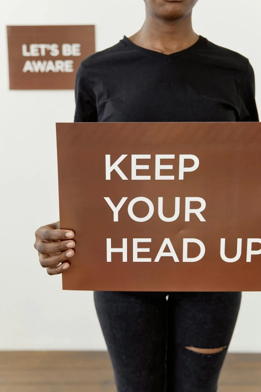 a woman holding a sign that says keep your head up, by Nina Hamnett, wearing a brown, ultra-high resolution, frontal shot, - i