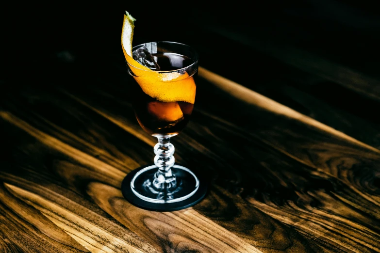 a drink sitting on top of a wooden table, by Carey Morris, unsplash, renaissance, cocktail in an engraved glass, long dark tattered umbra, tilt and orange, sasai ukon masanao