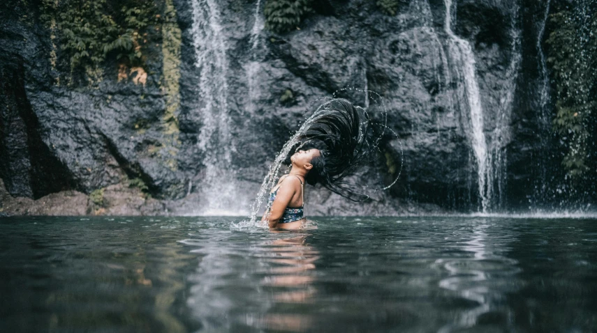 a woman standing in the water in front of a waterfall, by Jessie Algie, pexels contest winner, with aqua rapunzel dreadlocks, cindy avelino, swimming, heath clifford