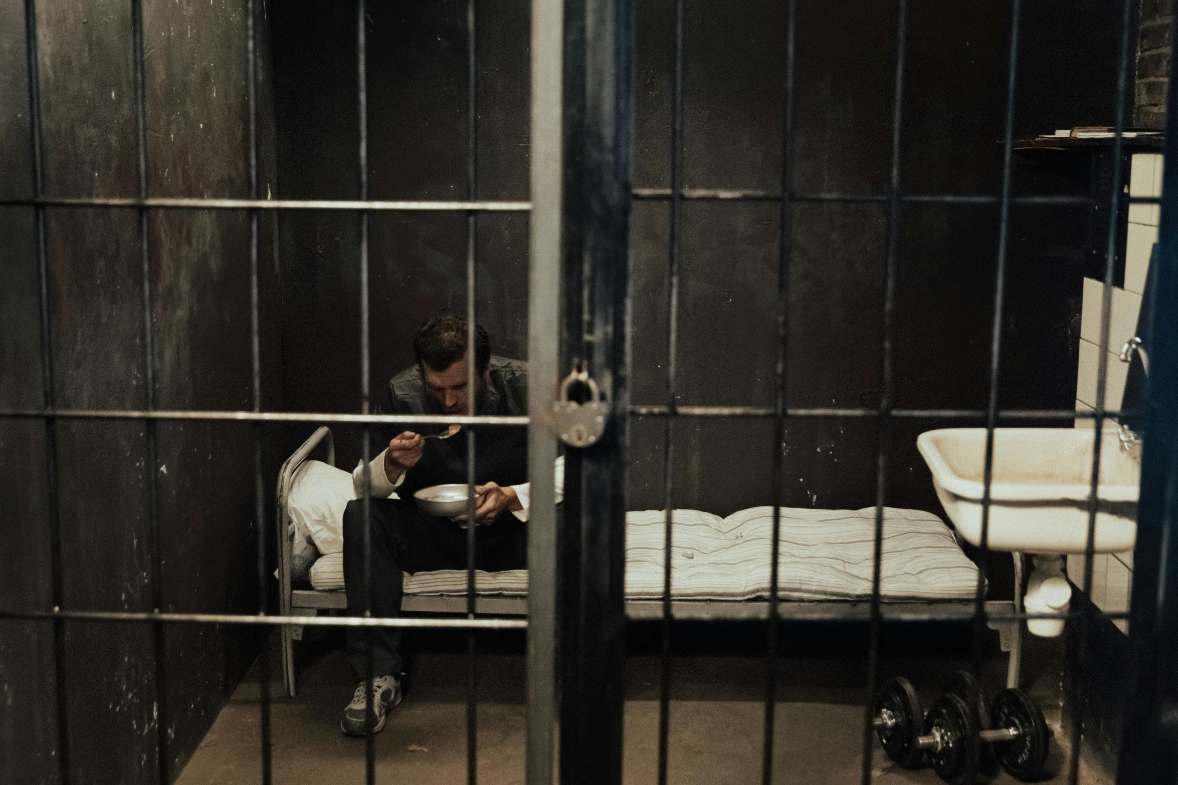 a man sitting on a bed in a jail cell, pexels contest winner, cell phone, instagram post, reading, handcuffed