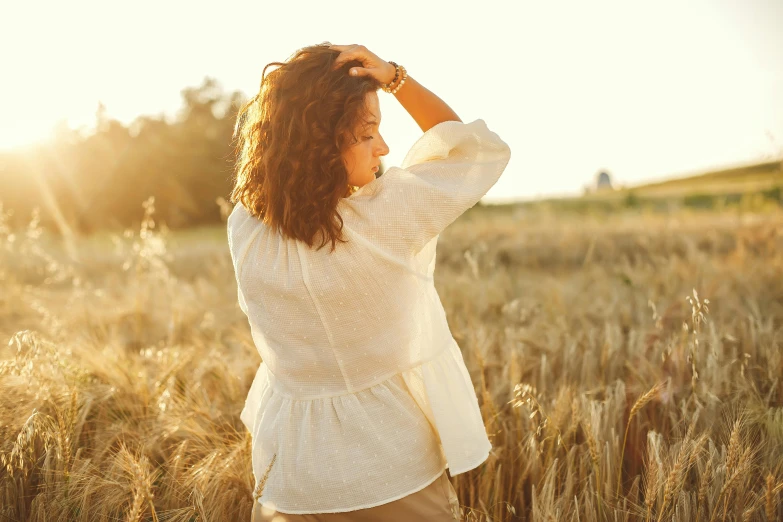 a woman standing in a field of wheat, trending on pexels, cream colored peasant shirt, frizzy hair, evening sunlight, brightly-lit