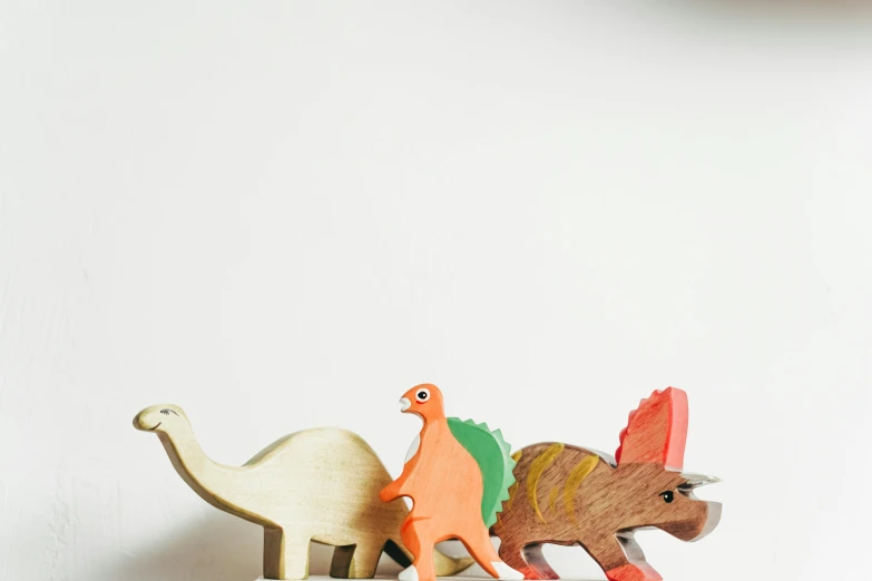 a close up of a toy dinosaur on a shelf, a jigsaw puzzle, by Adam Rex, trending on unsplash, figuration libre, wooden art toys on base, set against a white background, three animals, 1982