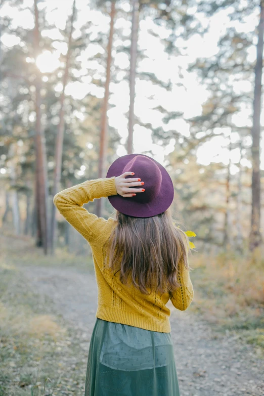 a woman wearing a purple hat standing in a forest, trending on unsplash, yellow hue, showing her shoulder from back, hand holding cap brim, instagram post