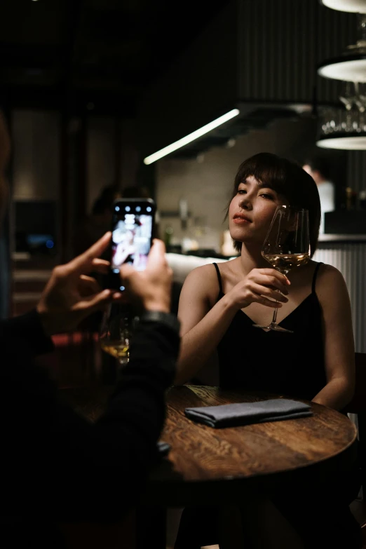 a man taking a picture of a woman holding a glass of wine, dark mood lighting, gen z, sitting at a table, multiple stories