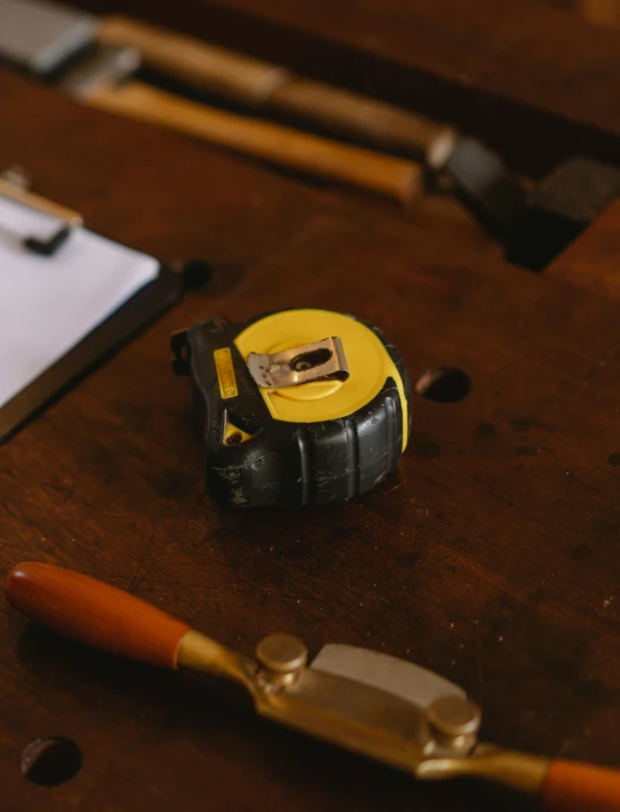 a yellow tape measure sitting on top of a wooden table, thumbnail, in a workshop, monocle, detailed product image