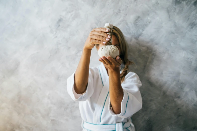 a woman holding a ball of yarn in front of her face, unsplash, renaissance, dressed as a pastry chef, white sarong, garlic on background, photoshoot for skincare brand