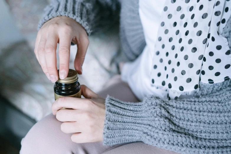 a woman sitting on top of a bed holding a bottle, by Julia Pishtar, trending on pexels, hibernation capsule close-up, manuka, carefully crafted, jar on a shelf