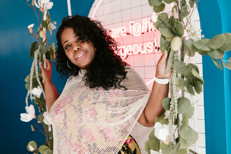 a woman standing in front of a blue wall, an album cover, by Dulah Marie Evans, featured on instagram, happening, wrapped in cables and flowers, smiling at camera, d. i. y. venue, curvaceous. detailed