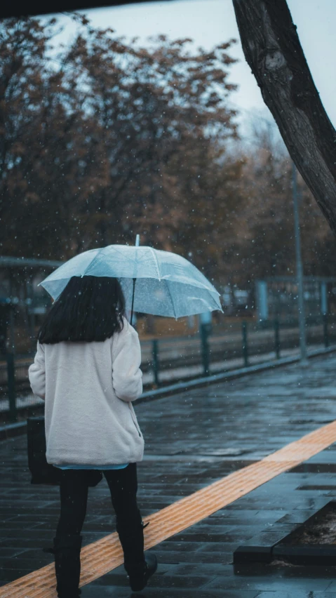 a woman holding an umbrella on a rainy day, inspired by Elsa Bleda, unsplash contest winner, realism, blue and gray colors, ☁🌪🌙👩🏾, sad lonely mellow vibes, instagram post