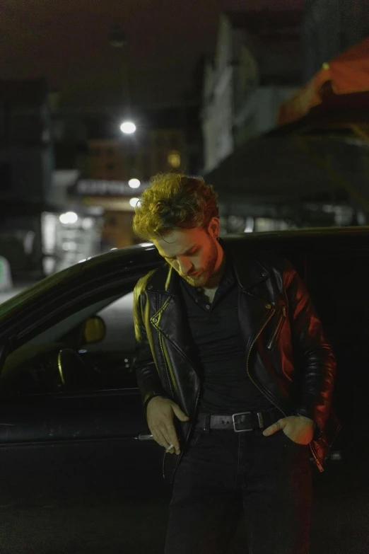 a man standing next to a car at night, an album cover, pexels, photorealism, leather jacket, charlie day, in sao paulo, cinestill eastmancolor