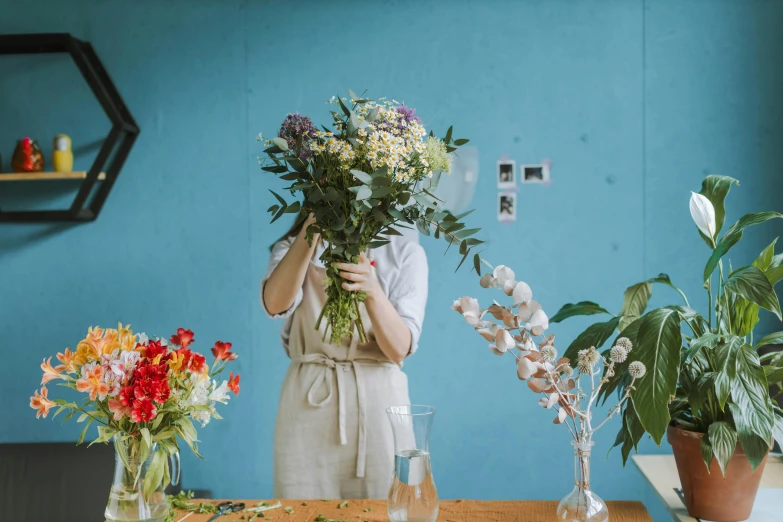 a woman holding a bunch of flowers in front of her face, a still life, trending on unsplash, artist wearing overalls, vases and bottles, brown and cyan blue color scheme, in a workshop