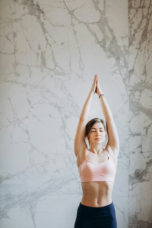 a woman doing a yoga pose in front of a marble wall, pexels contest winner, health supporter, raised hand, low quality photo, religious