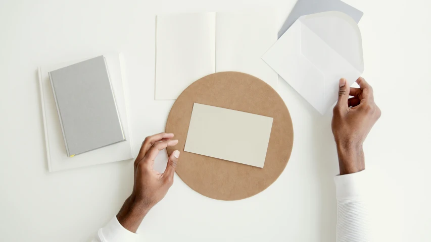 a person holding a piece of paper on top of a table, private press, sleek round shapes, flatlay, cardboard, card frame