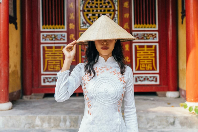 a woman wearing a hat standing in front of a building, inspired by Tan Ting-pho, pexels contest winner, cloisonnism, authentic costume, white, religious, 1 2 9 7