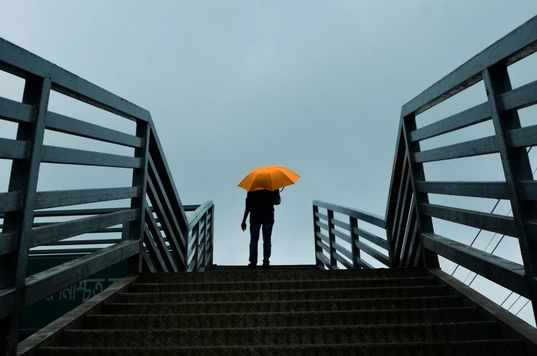 a person with an umbrella standing on a set of stairs, a picture, unsplash, vibrant but dreary orange, grey sky, concerned, viewed from the ground