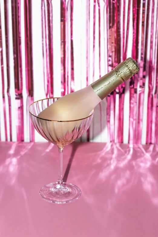 a bottle of champagne in a glass on a table, by Alice Mason, happening, pink background, disco party, feature, aged 2 5