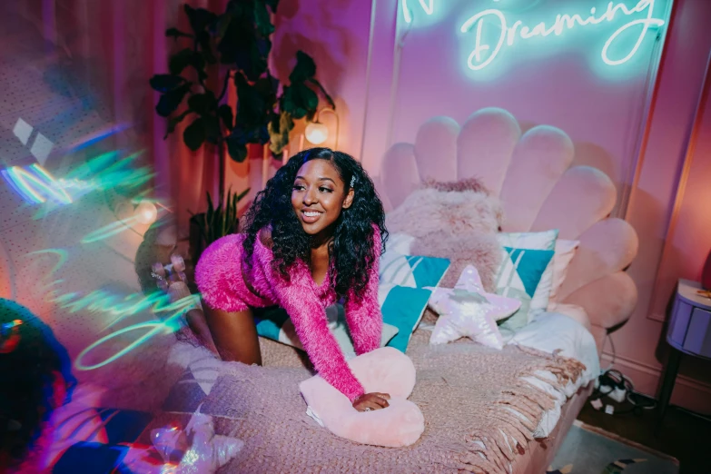 a woman sitting on a bed in front of a neon sign, an album cover, trending on pexels, happening, turquoise and pink lighting, black young woman, dreamcore looking, in the bedroom at a sleepover