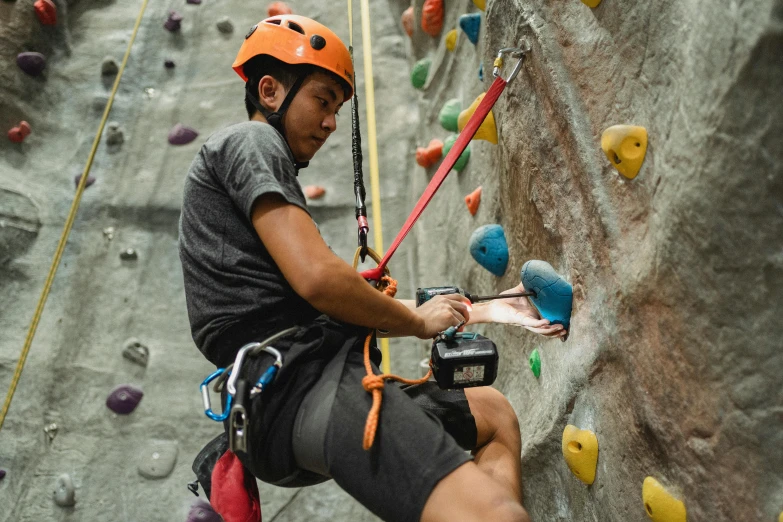 a man climbing up the side of a rock wall, pexels contest winner, wearing skating helmet, avatar image, indoor picture, asian male
