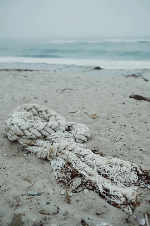 a rope laying on top of a sandy beach, unsplash, land art, white braids, dressed in a worn, hollister ranch, in the ocean