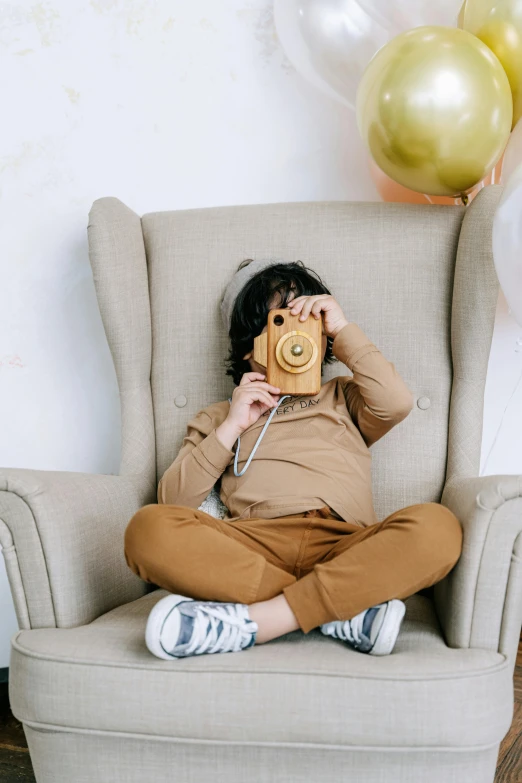 a person sitting in a chair holding a camera, a picture, toddler, brown clothes, armchairs, kids