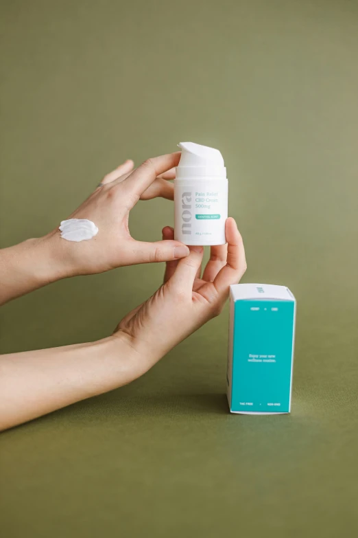 a person holding a bottle of lotion next to a bottle of lotion, inspired by Eero Snellman, happening, white and teal garment, dynamic angled shot, label, silicone skin