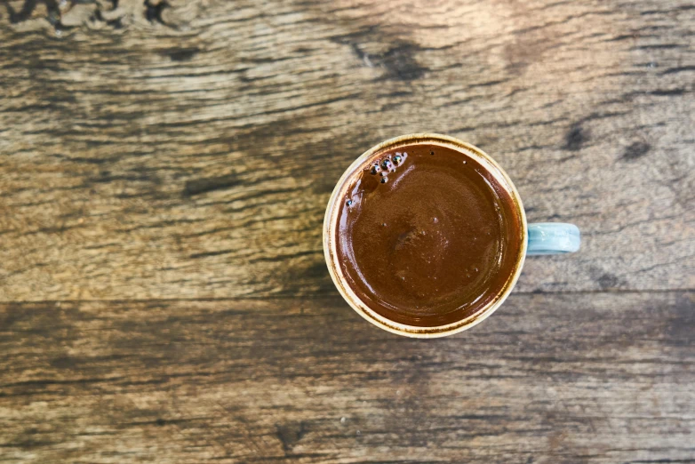 a cup of coffee sitting on top of a wooden table, smothered in melted chocolate, jen atkin, top-down shot, detailed product image