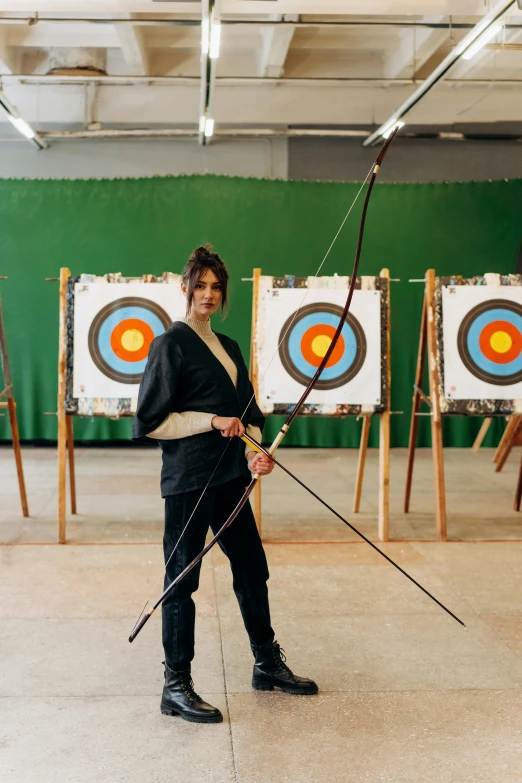 a man that is standing in front of a bunch of arrows, a portrait, by Marina Abramović, pexels contest winner, woman holding recurve bow, in a dojo, standing in an arena, elizabeth saltzman