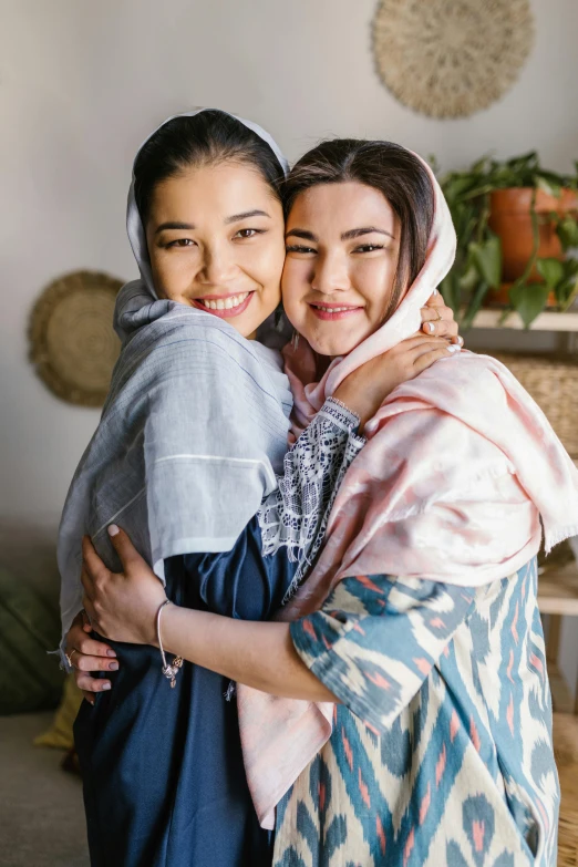 two women hugging each other in a living room, inspired by Maryam Hashemi, hurufiyya, promo image, close up portrait shot, wearing simple robes, friends