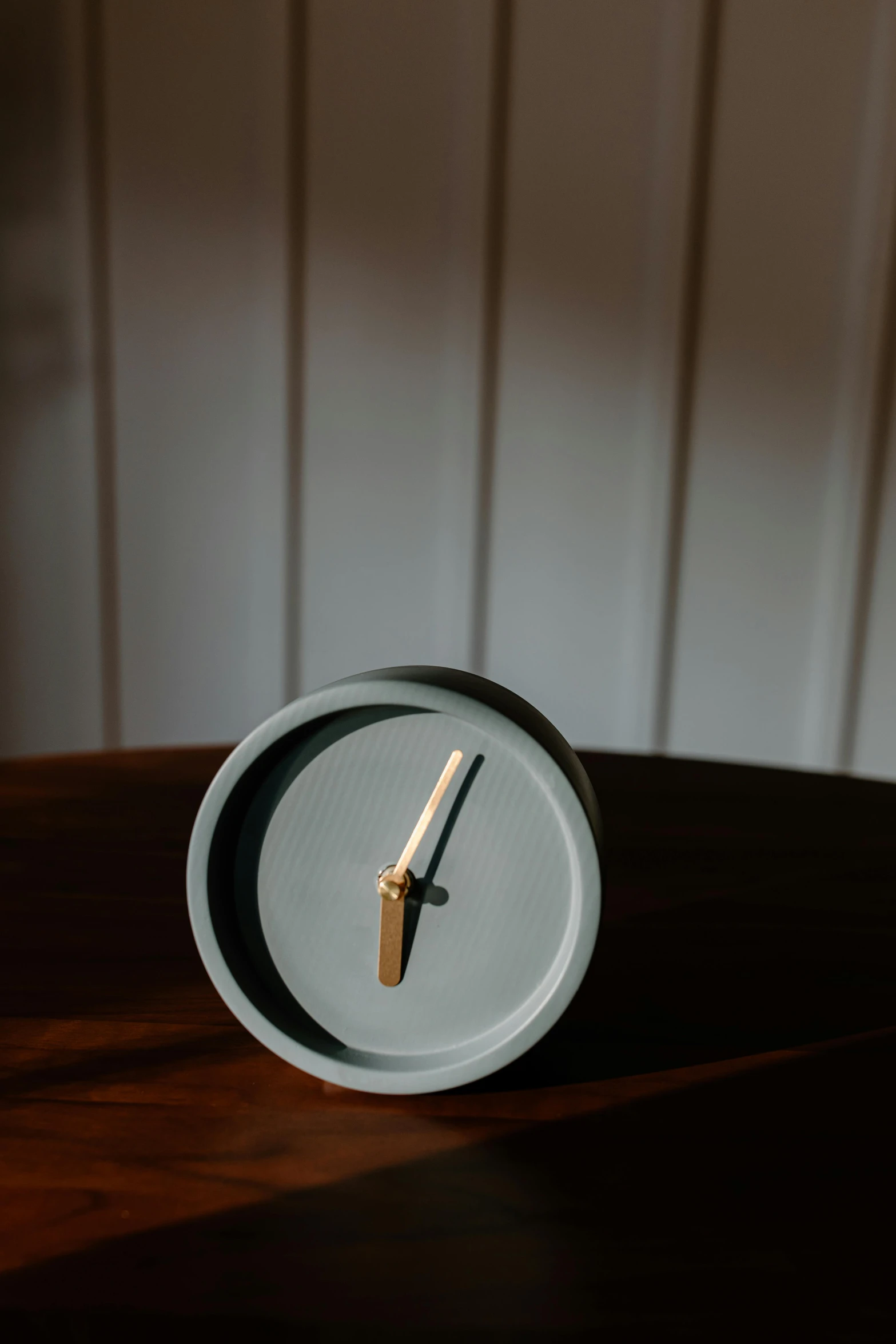 a clock sitting on top of a wooden table, in gunmetal grey, dwell, light grey blue and golden, round-cropped