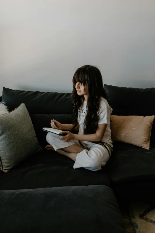 a girl sitting on a couch reading a book, a child's drawing, by Robbie Trevino, pexels contest winner, happening, asian girl with long hair, wearing a tee shirt and combats, writing in journal, cinematic outfit photo