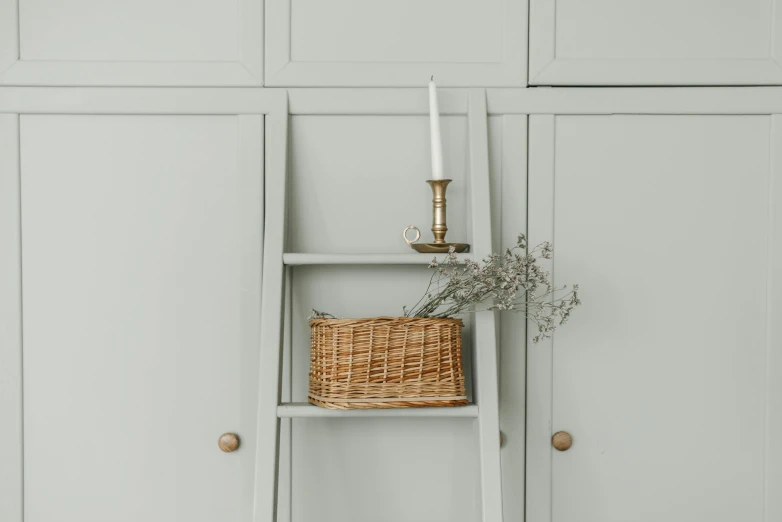 a ladder with a wicker basket on top of it, a still life, inspired by Rachel Whiteread, arts and crafts movement, sage green, cupboards, close-up product photo, holding a candle holder