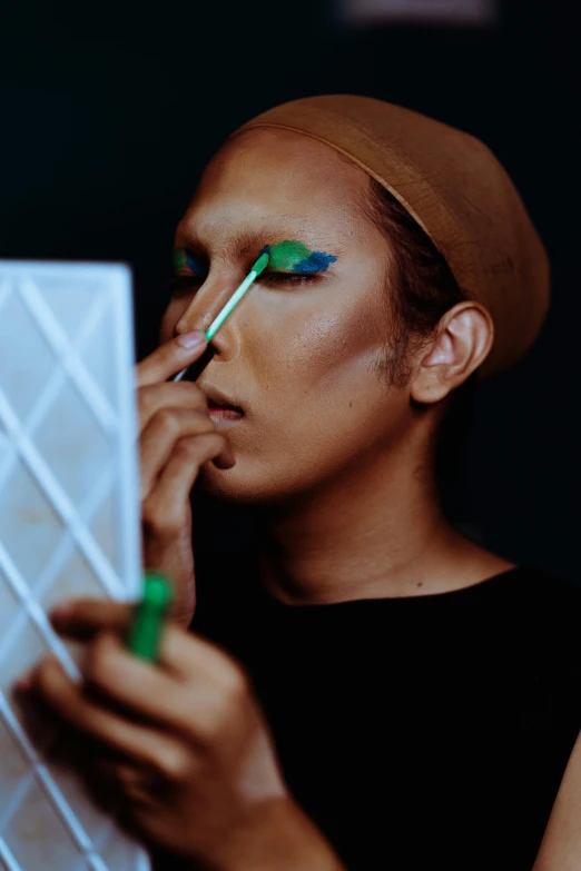 a woman putting on makeup in front of a mirror, an album cover, inspired by Yanagawa Nobusada, unsplash, male model, green and blue, malaysian, avant garde fashion model